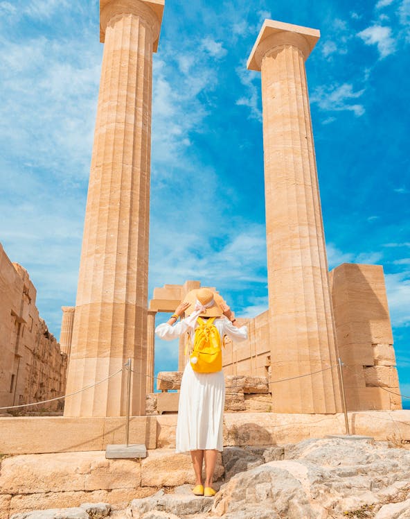 Traveler exploring ancient columns at the Acropolis of Lindos, Greece.