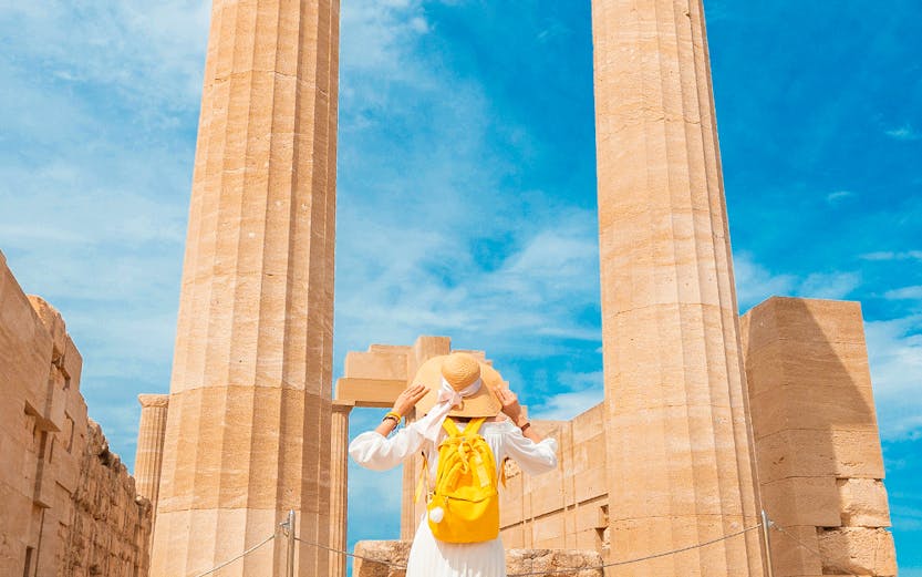 Traveler exploring ancient columns at the Acropolis of Lindos, Greece.