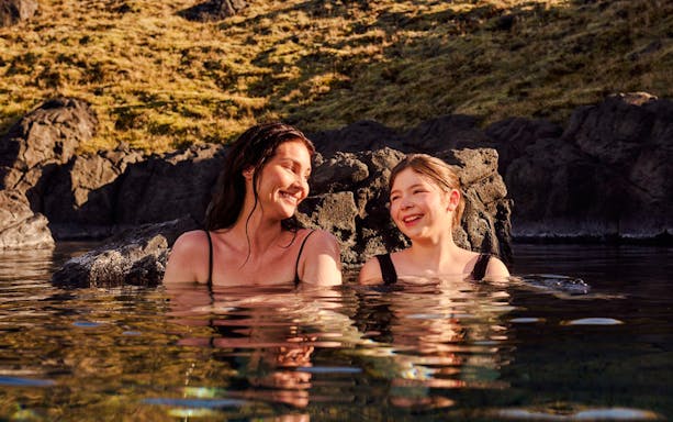 Guests enjoying the warm waters at Sky Lagoon, surrounded by rocky landscape.