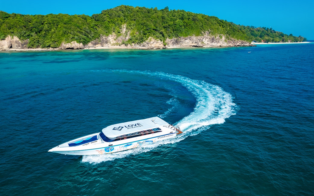 Speed boat cruising towards Similan Island with lush green coastline in the background.