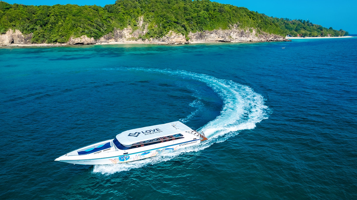Speed boat cruising towards Similan Island with lush green coastline in the background.