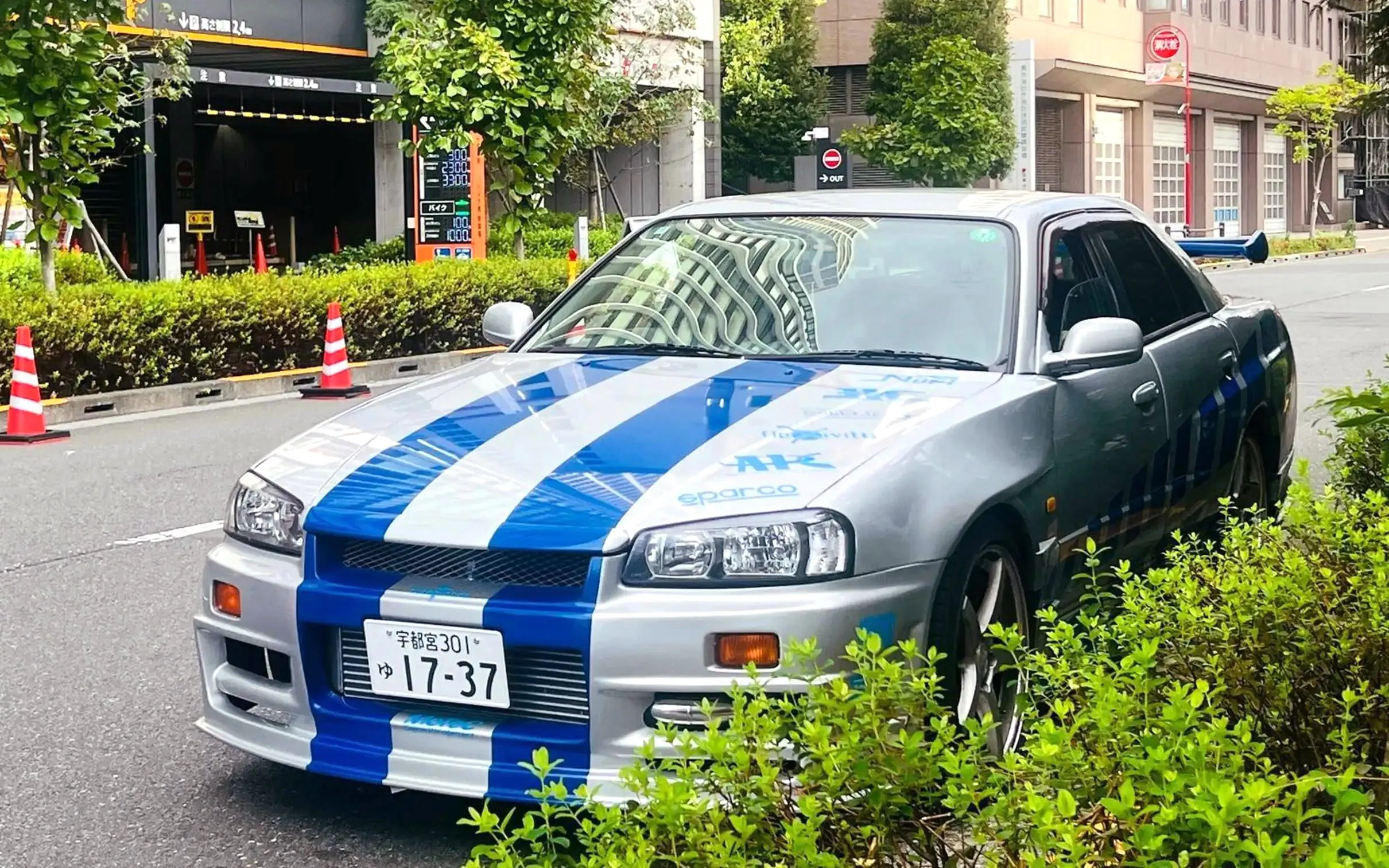Silver sports car with blue racing stripes parked on a Tokyo street, part of the Tokyo Drift 5.0 experience.