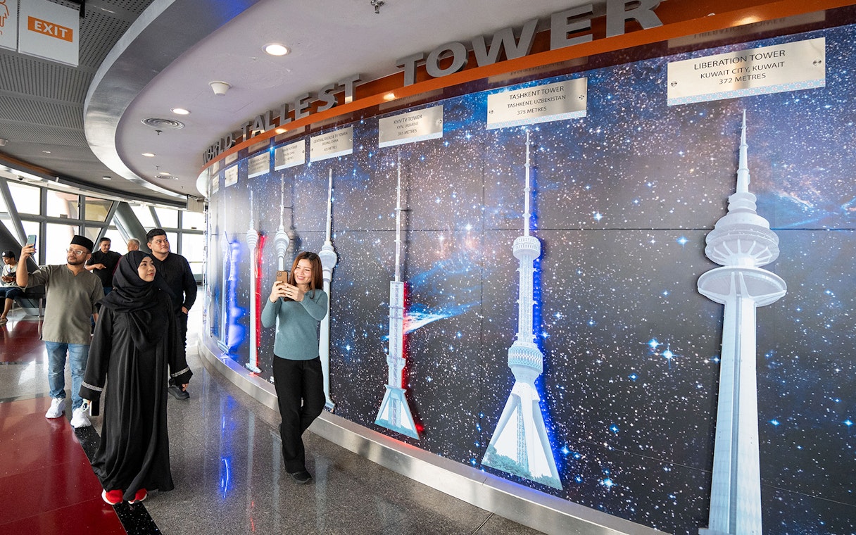 Tourists at Kuala Lumpur Tower Observation Deck viewing tower models display.
