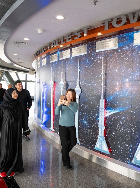 Tourists at Kuala Lumpur Tower Observation Deck viewing tower models display.