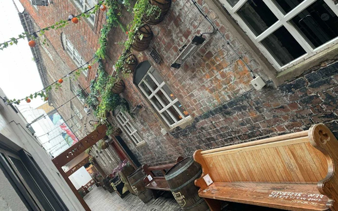 Narrow alleyway in Belfast with hanging plants and benches, part of the Ghosts of Belfast exploration game.