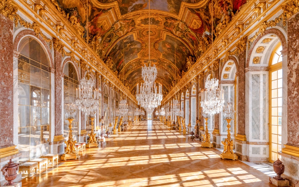 Gallery of Mirrors in Versailles Palace, Paris, showcasing ornate chandeliers and reflective mirrors.