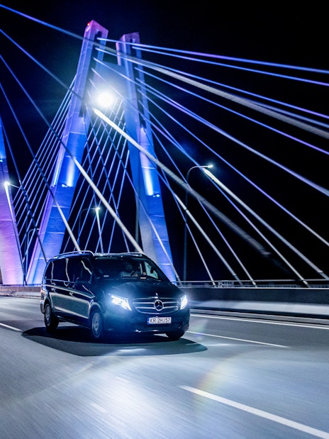 Private transfer car crossing illuminated bridge at night in Krakow.