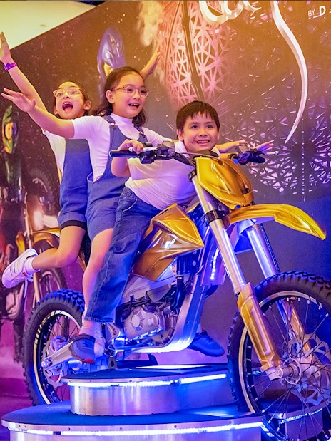 Children posing on a display motorcycle at La Perle by Dragone in Dubai.