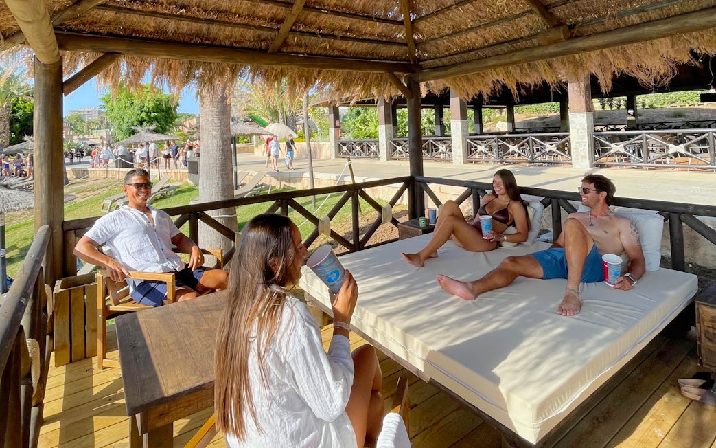 Resting area at Banana lounge, Aqualand Torremolinos, with people relaxing under a thatched roof.
