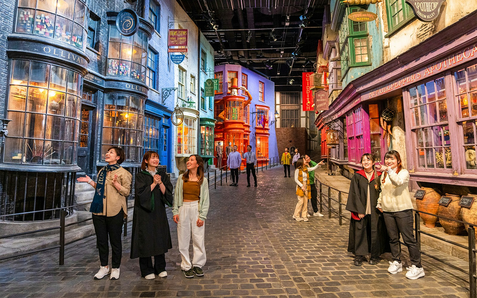 People exploring Diagon Alley with colorful shopfronts and cobblestone street.