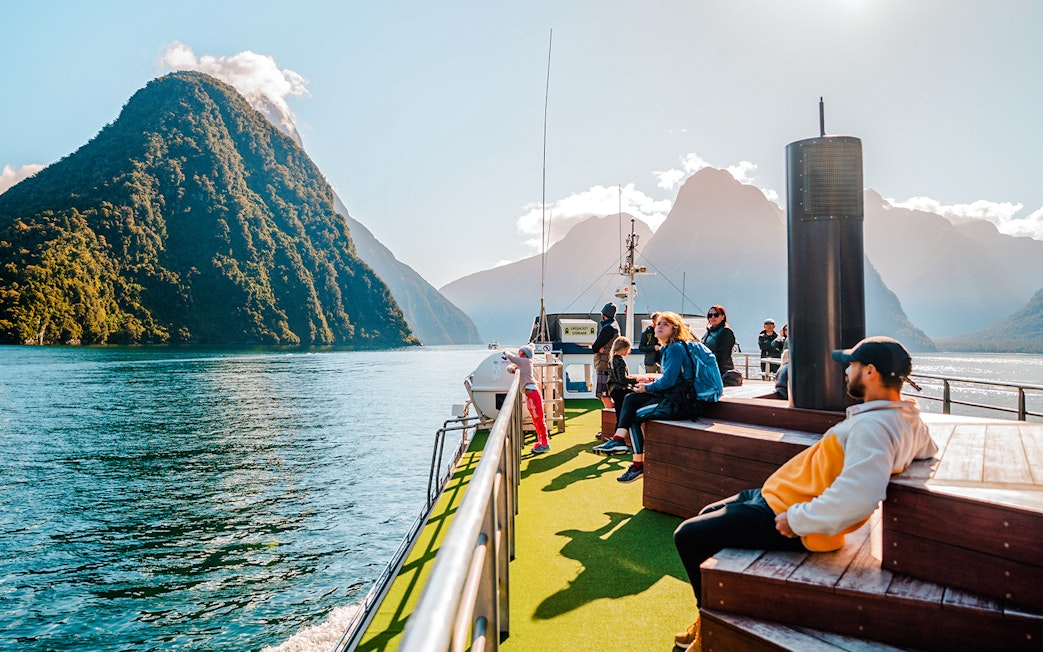 People enjoying a boat tour on Milford Sound, New Zealand, with scenic mountain views.