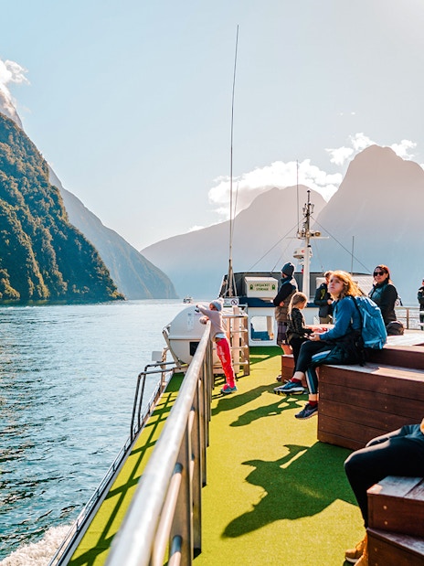 People enjoying a boat tour on Milford Sound, New Zealand, with scenic mountain views.