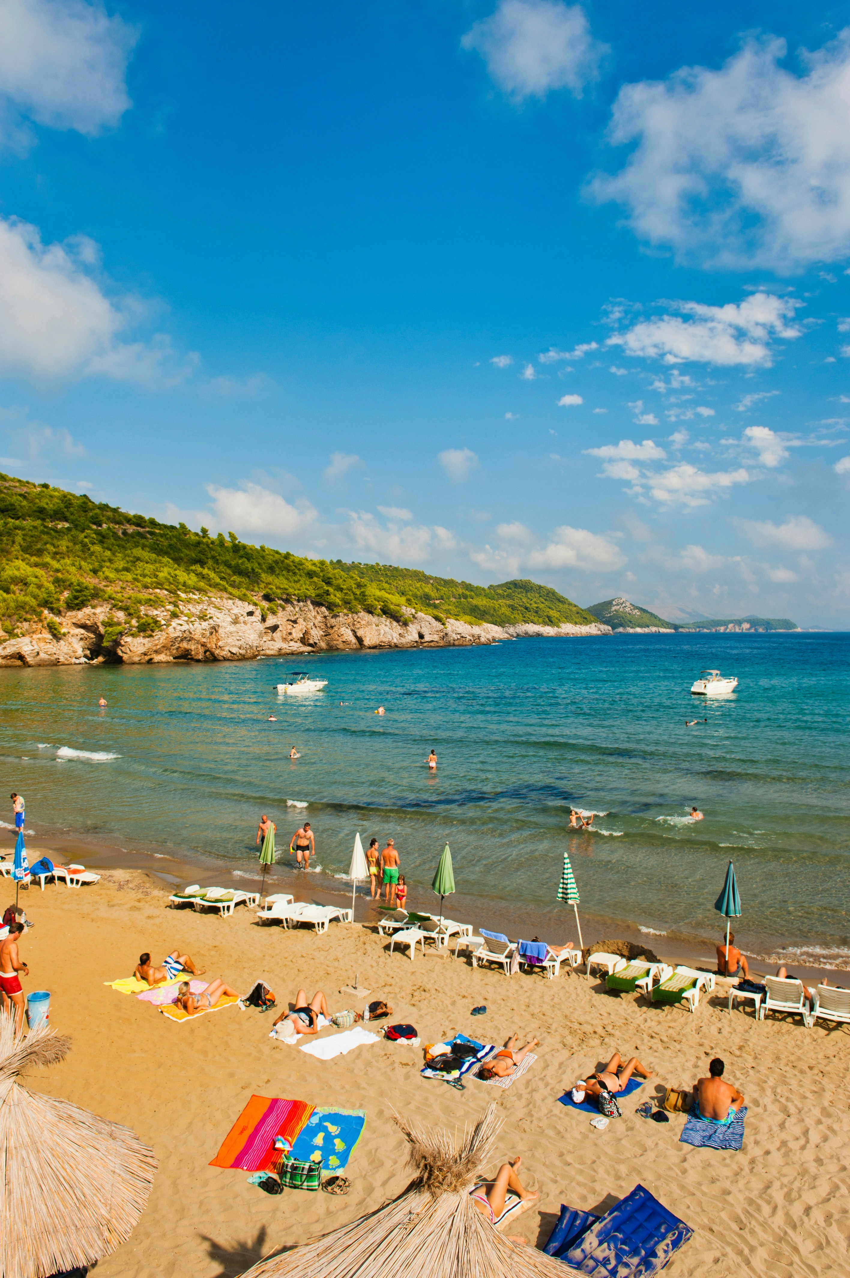Tourists relaxing on Sunj Beach, Lopud Island, Croatia, with clear blue waters and lush greenery in the background.