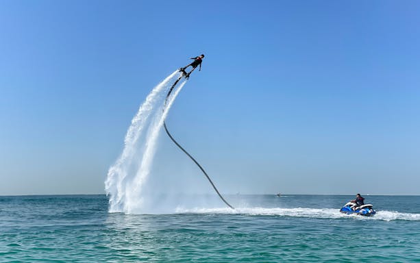 Flyboarding over the sea in Dubai with a jet ski nearby.