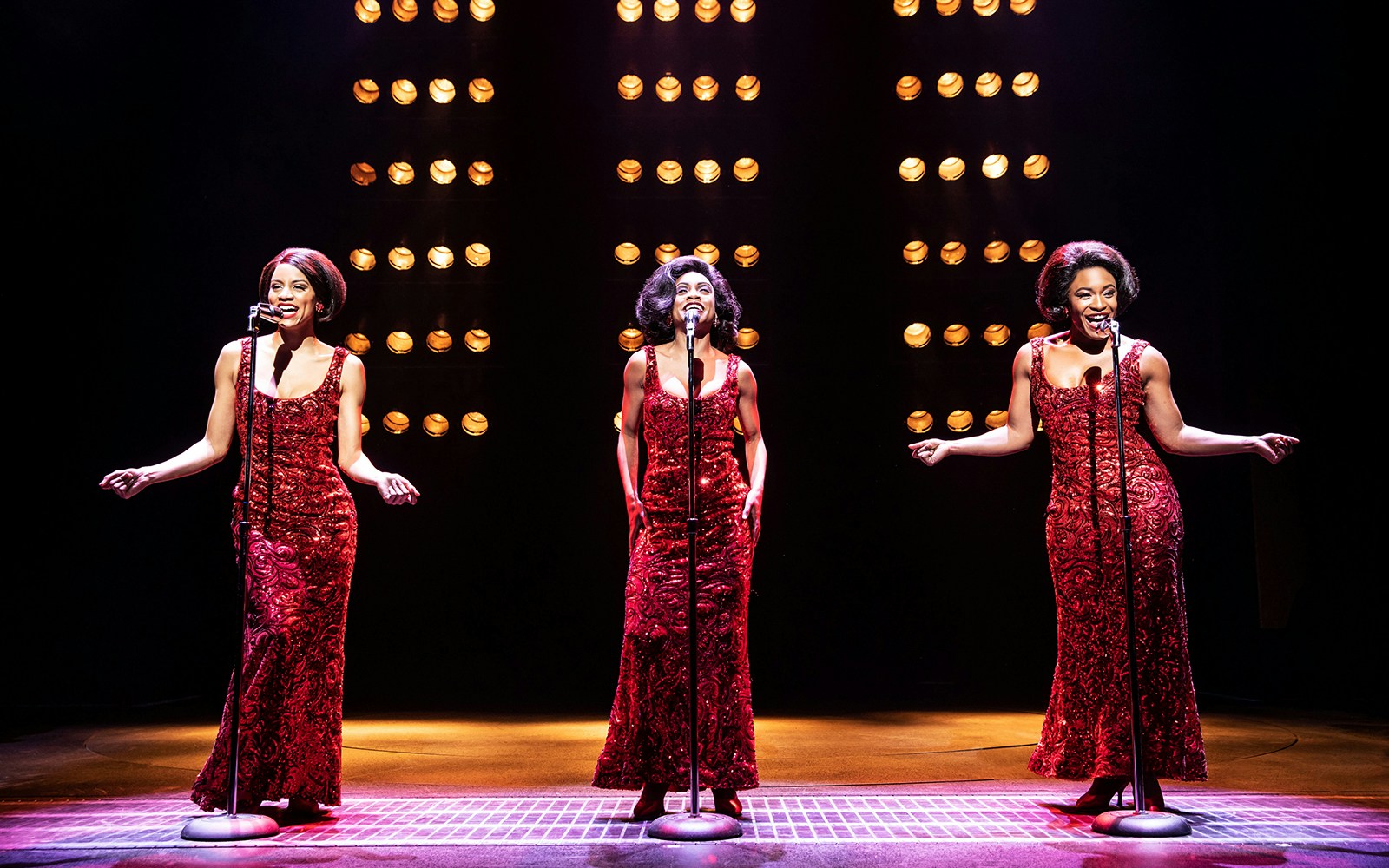 Performers in red dresses singing on stage during "Ain't Too Proud" musical.
