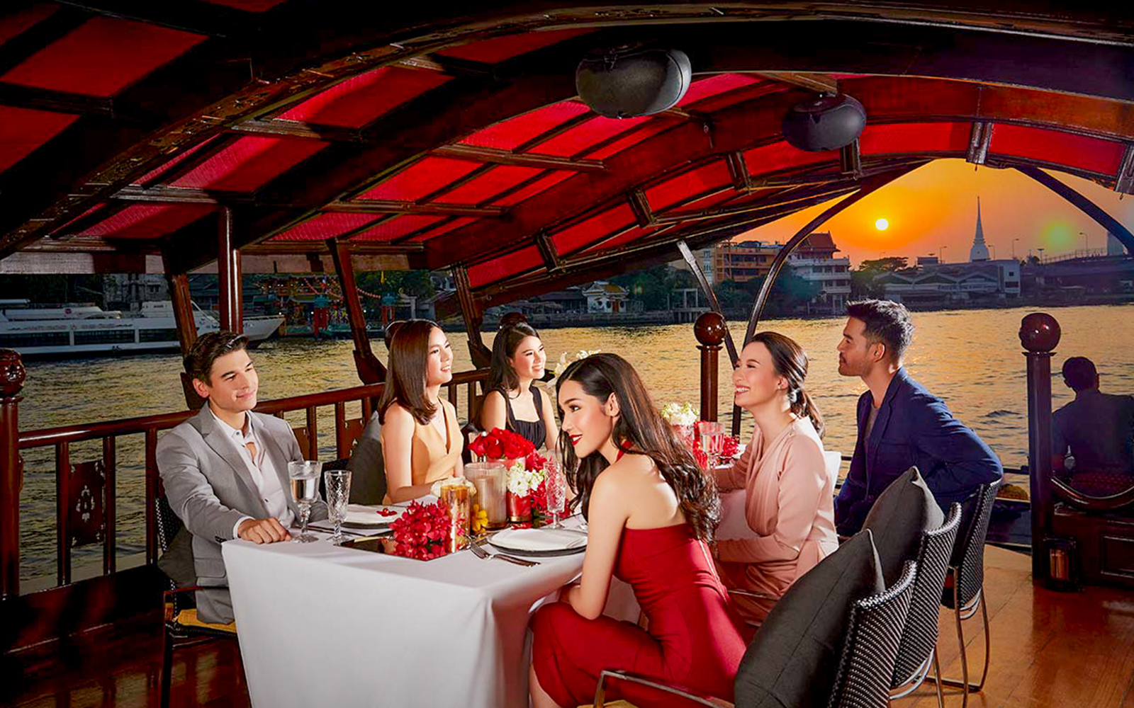 Guests dining on the Manohra Dinner Cruise at sunset on the Chao Phraya River, Bangkok.