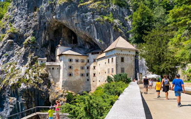 Predjama Castle built into a cliff with tourists walking nearby, Slovenia.