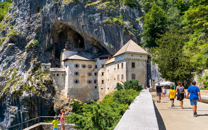 Predjama Castle built into a cliff with tourists walking nearby, Slovenia.