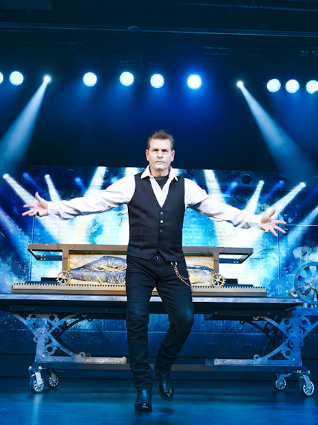 Magician performing on stage with assistant during Evolution Magic Show.