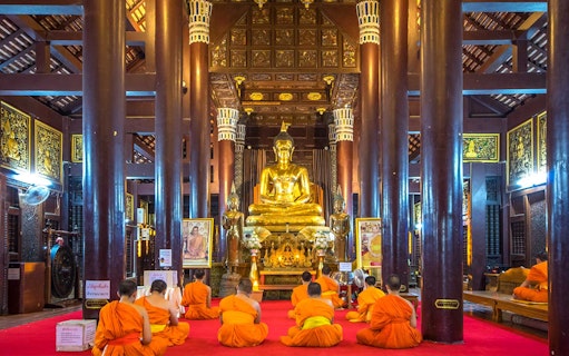 Monks meditating in front of a golden Buddha statue in a Chiang Mai temple.