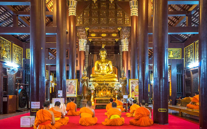 Monks meditating in front of a golden Buddha statue in a Chiang Mai temple.