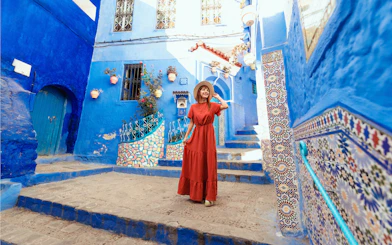 Young woman in red dress exploring blue streets of Chefchaouen, Morocco.