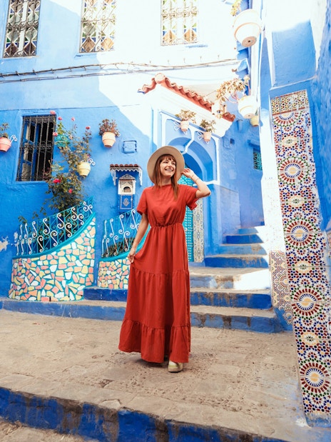 Young woman in red dress exploring blue streets of Chefchaouen, Morocco.