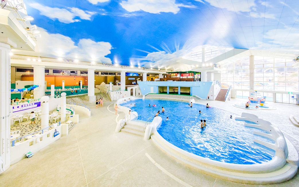 People swimming in the indoor pool at Hakone Kowakien Yunessun, Japan, under a sky-painted ceiling.