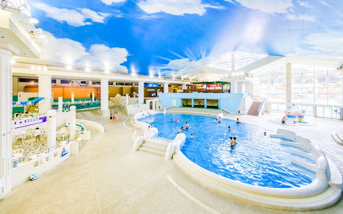 People swimming in the indoor pool at Hakone Kowakien Yunessun, Japan, under a sky-painted ceiling.