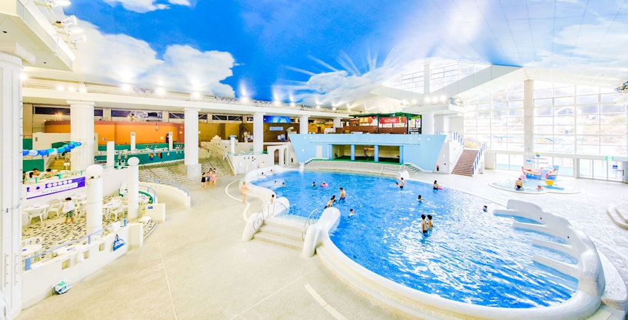 People swimming in the indoor pool at Hakone Kowakien Yunessun, Japan, under a sky-painted ceiling.