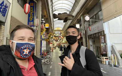 Visitors exploring a covered shopping street in Osaka with traditional lanterns and signs.