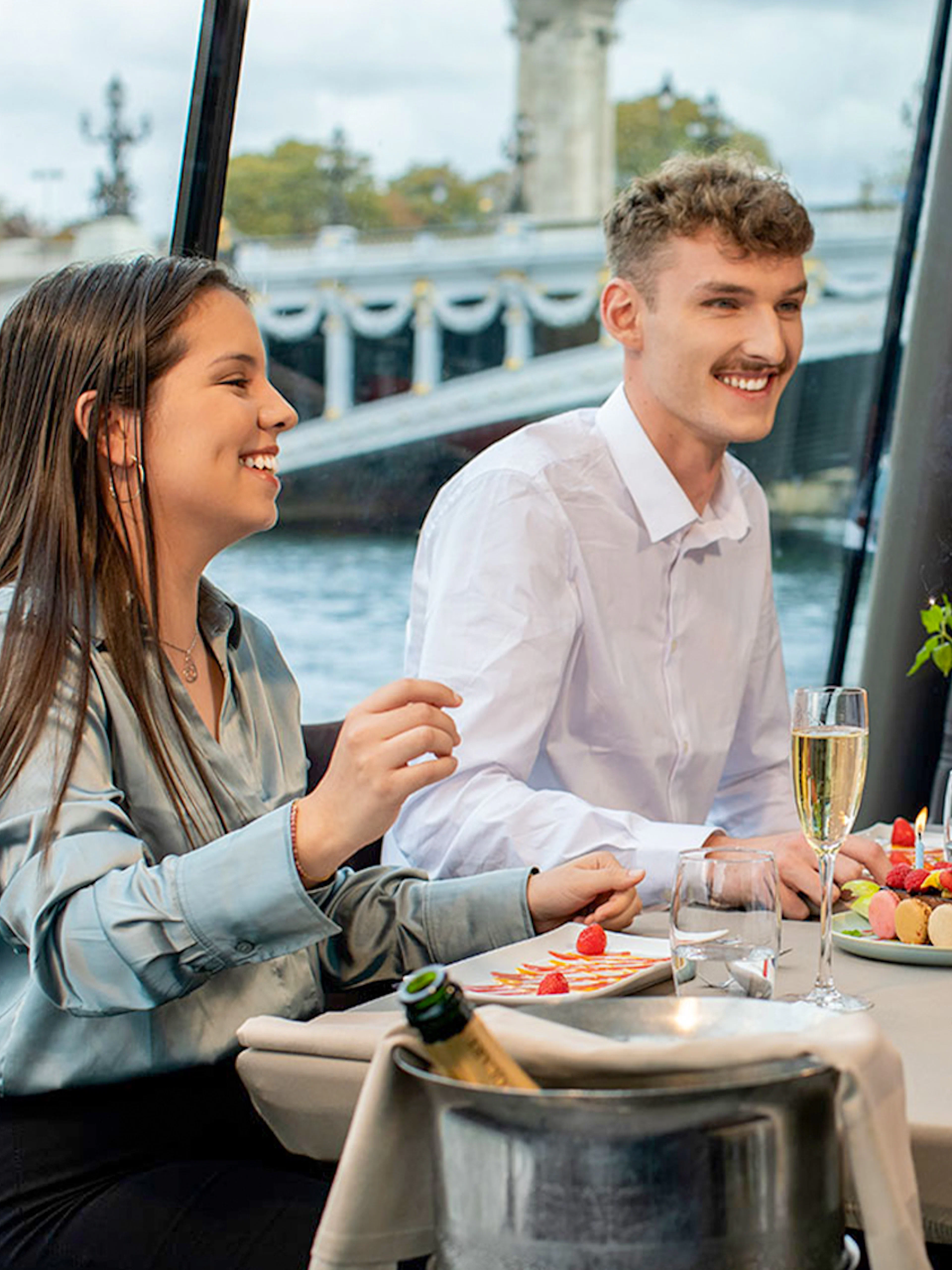 People dining on a Seine River lunch cruise in Paris with a view of a bridge.