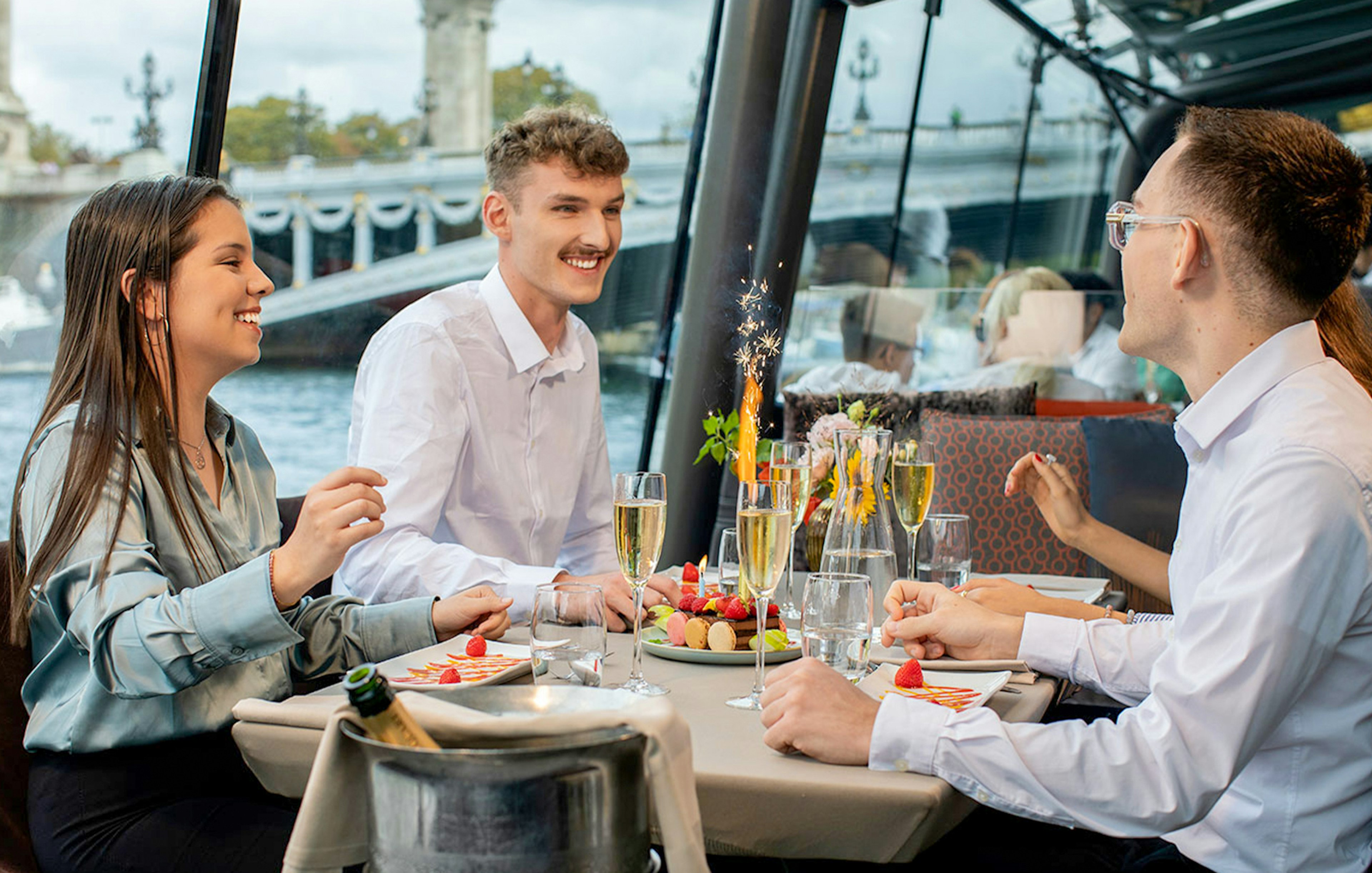 People dining on a Seine River lunch cruise in Paris with a view of a bridge.