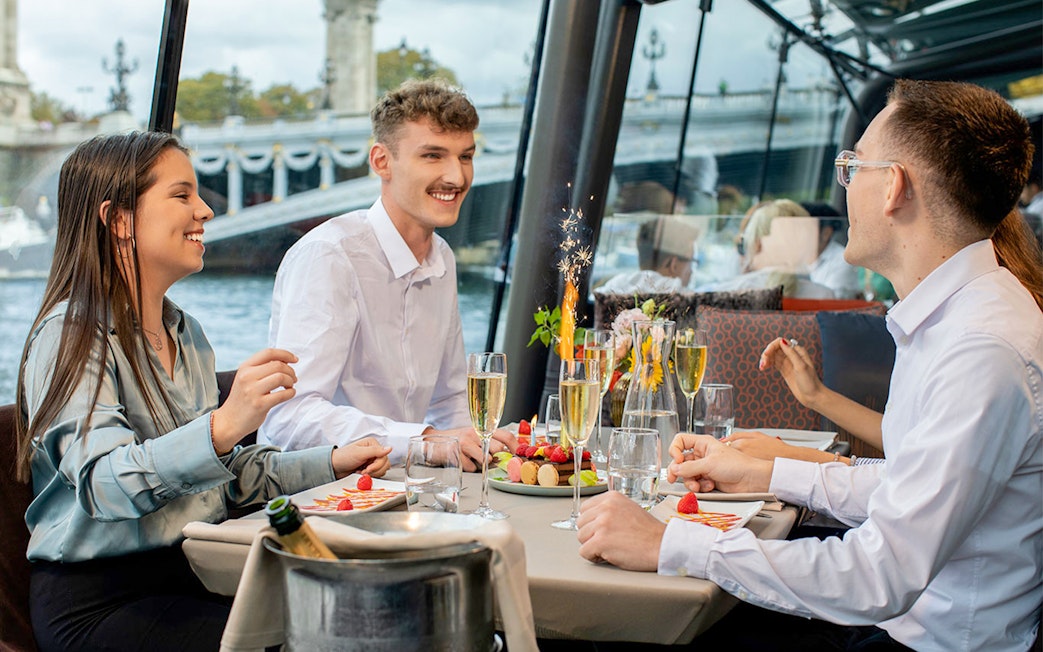 People dining on a Seine River lunch cruise in Paris with a view of a bridge.