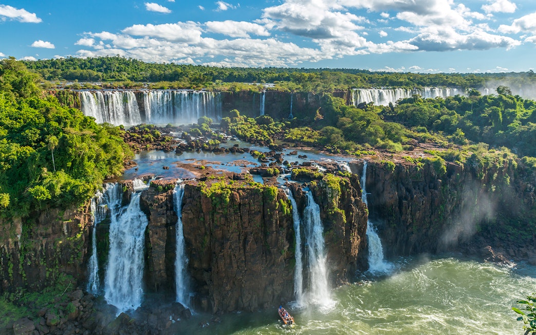 Iguazu Falls cascading over lush cliffs in Argentina, with a boat approaching the base.