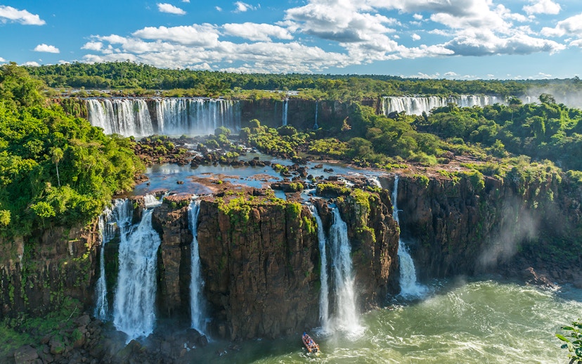 Iguazu Falls cascading over lush cliffs in Argentina, with a boat approaching the base.