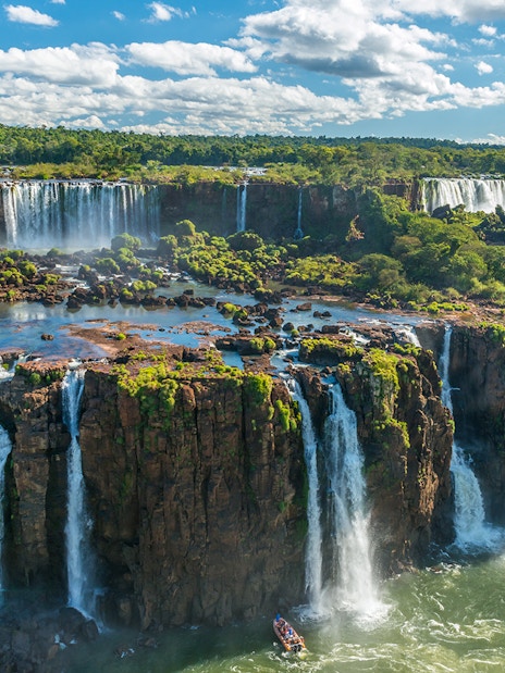 Iguazu Falls cascading over lush cliffs in Argentina, with a boat approaching the base.