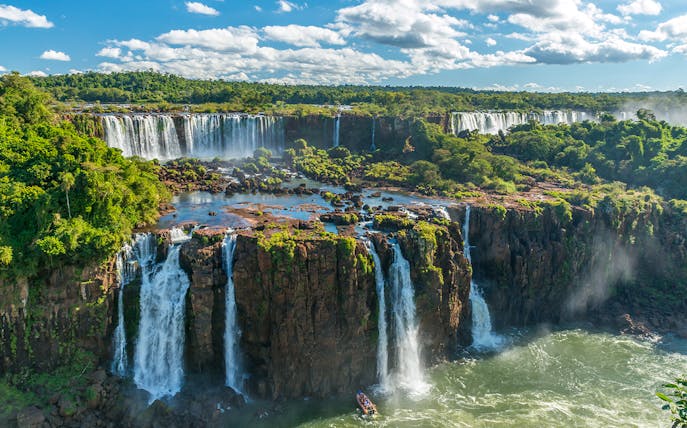 Iguazu Falls cascading over lush cliffs in Argentina, with a boat approaching the base.