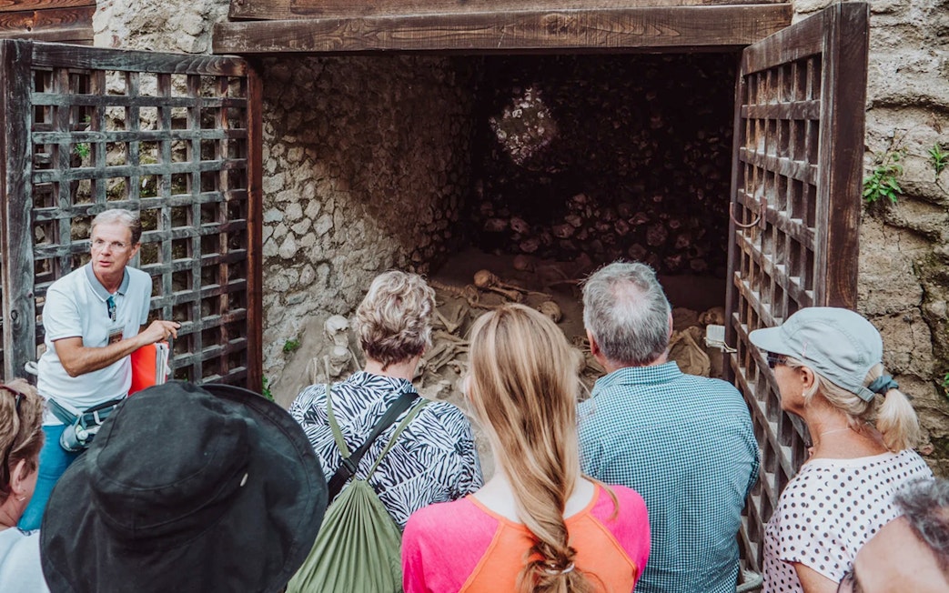 Tour group with archaeologist at Herculaneum site viewing ancient skeletons.