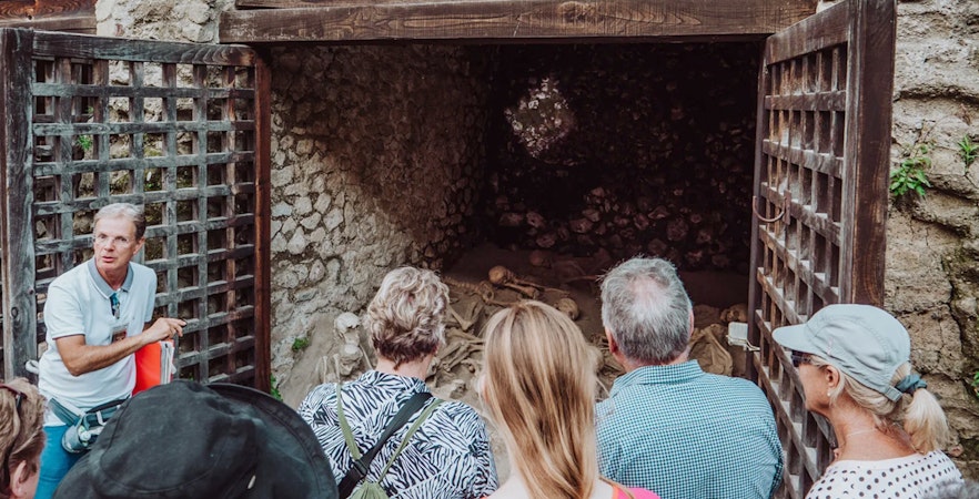 Tour group with archaeologist at Herculaneum site viewing ancient skeletons.