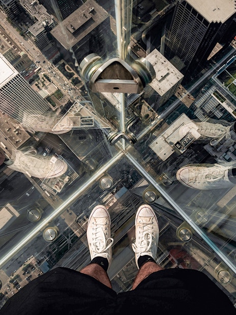 Guests standing on Chicago Skydeck glass ledge overlooking cityscape during architecture tour.