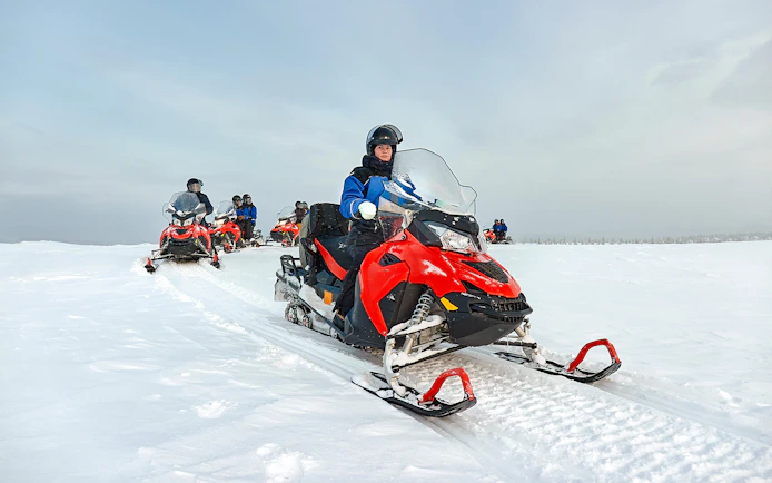 Snowmobile group riding through snowy landscape in Lapland.