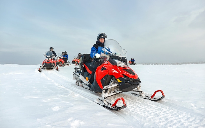Snowmobile group riding through snowy landscape in Lapland.