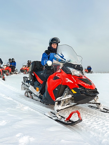 Snowmobile group riding through snowy landscape in Lapland.
