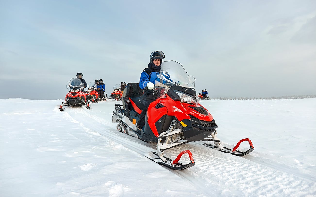 Snowmobile group riding through snowy landscape in Lapland.