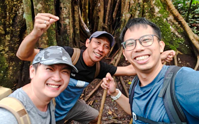 Trekkers smiling in front of large tree roots during Bali jungle trek.