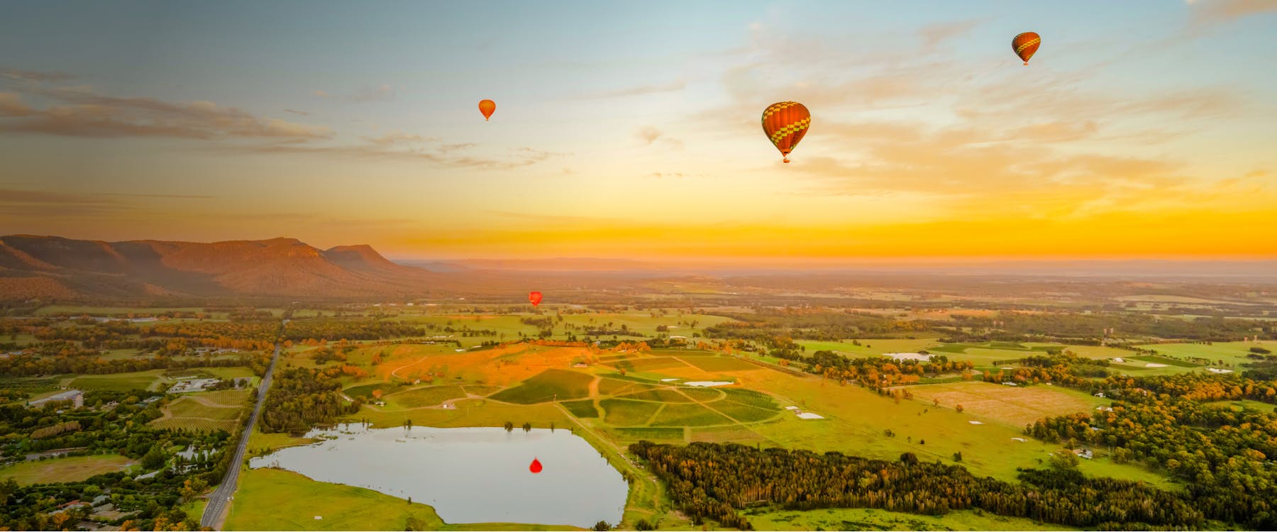 Hot air balloons floating over vineyards and fields at sunrise in Pokolbin, Australia.