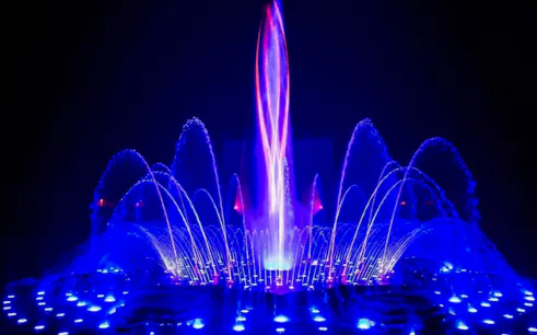 Fountain light show at Akshardham Temple, Agra, with vibrant blue and purple water jets.