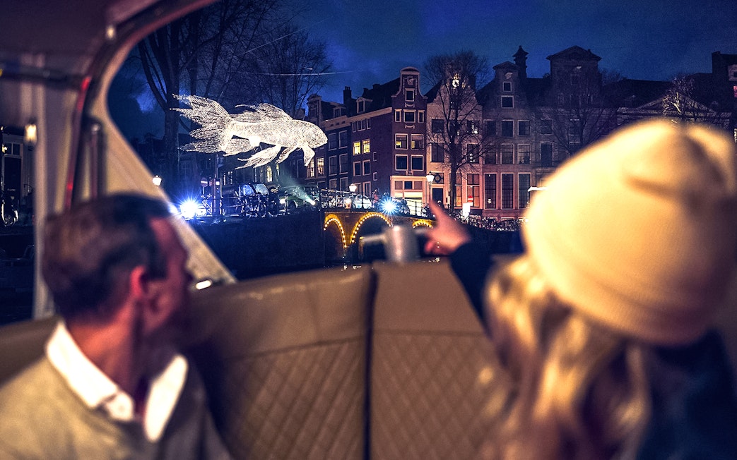 Canal view of illuminated fish sculpture during Amsterdam Light Festival cruise.