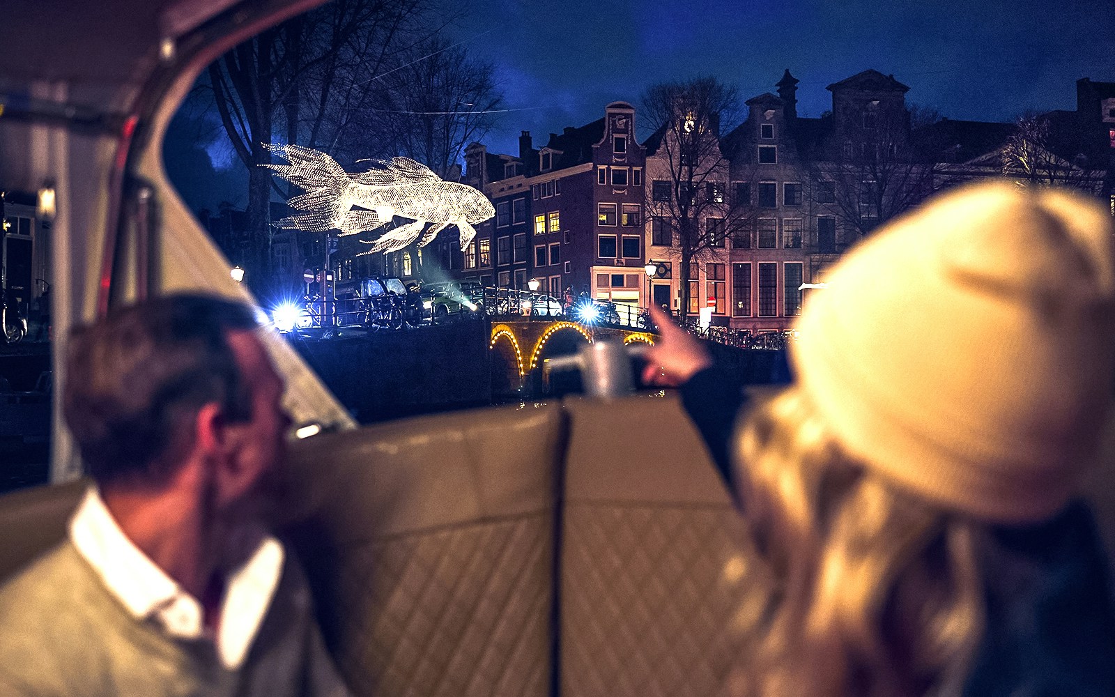 Canal view of illuminated fish sculpture during Amsterdam Light Festival cruise.